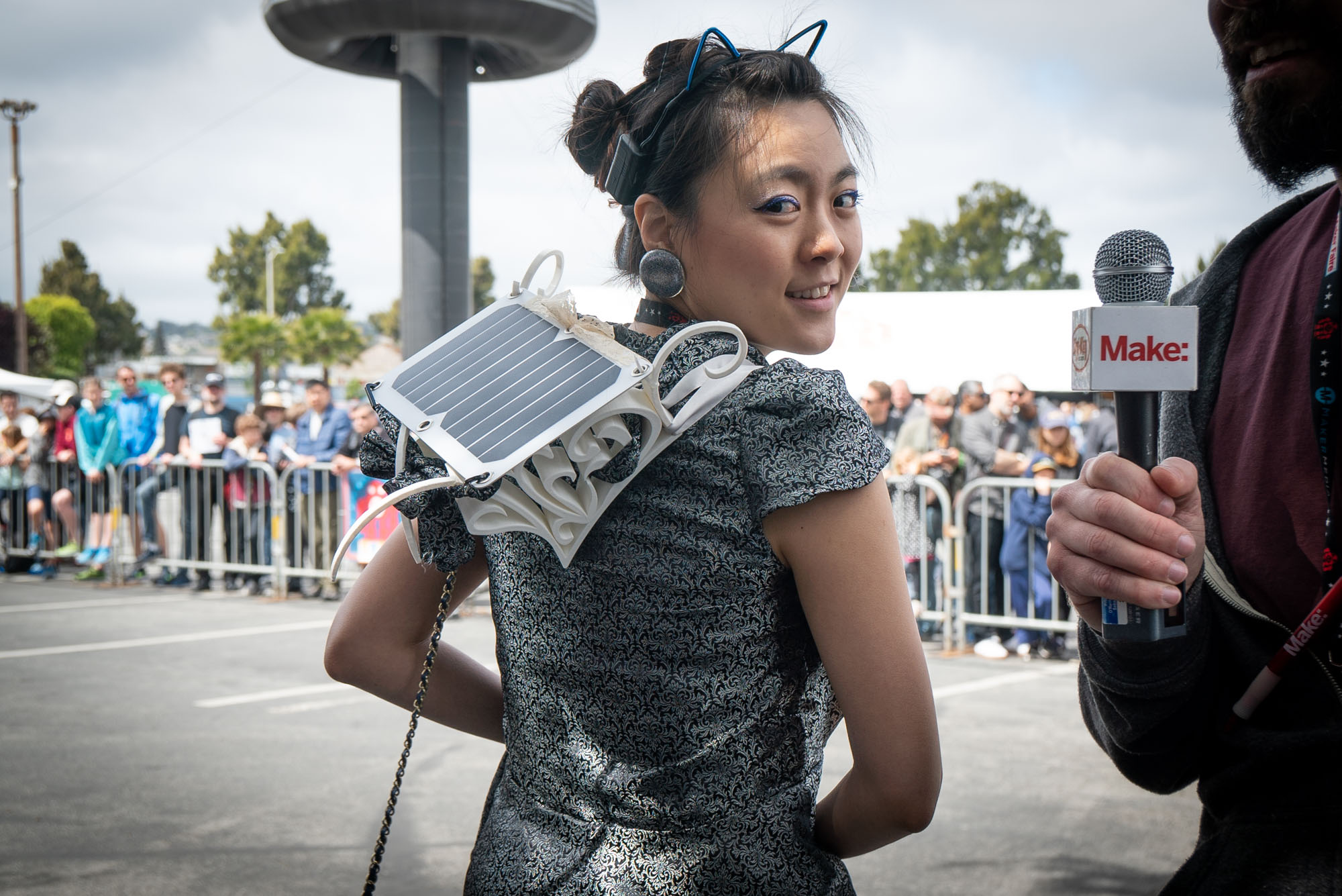 Kitty Yeung stands with her back to the camera looking over one shoulder, displaying her 3D printed solar panel wearable recharging station on her back.